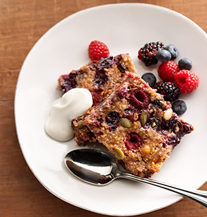 Fruity Crunch Baked Oatmeal made with Astro Yogurt on a white plate with blueberries, raspberries, blackberries and a dollap of yogurt on the side.