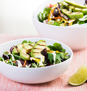 Avocado Dressing made with Astro yogurt and drizzled on a green salad with avocado slices and a wedge of lime on the side