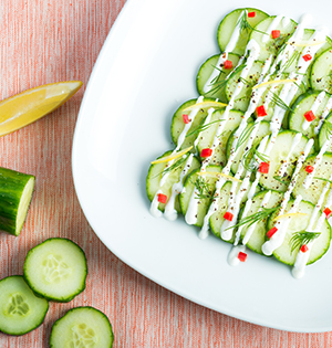 Cucumber Salad made with Astro yogurt served on a white plate beside cucumber slices and a wedge of lemon