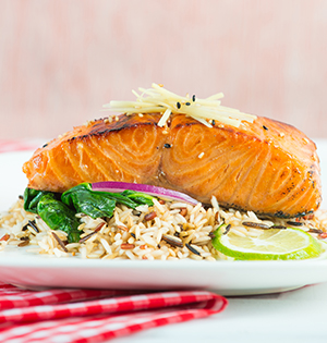Ginger Soy Glazed Salmon made with Astro yogurt served on a white place with rice and spinach on the side and a slice of lime